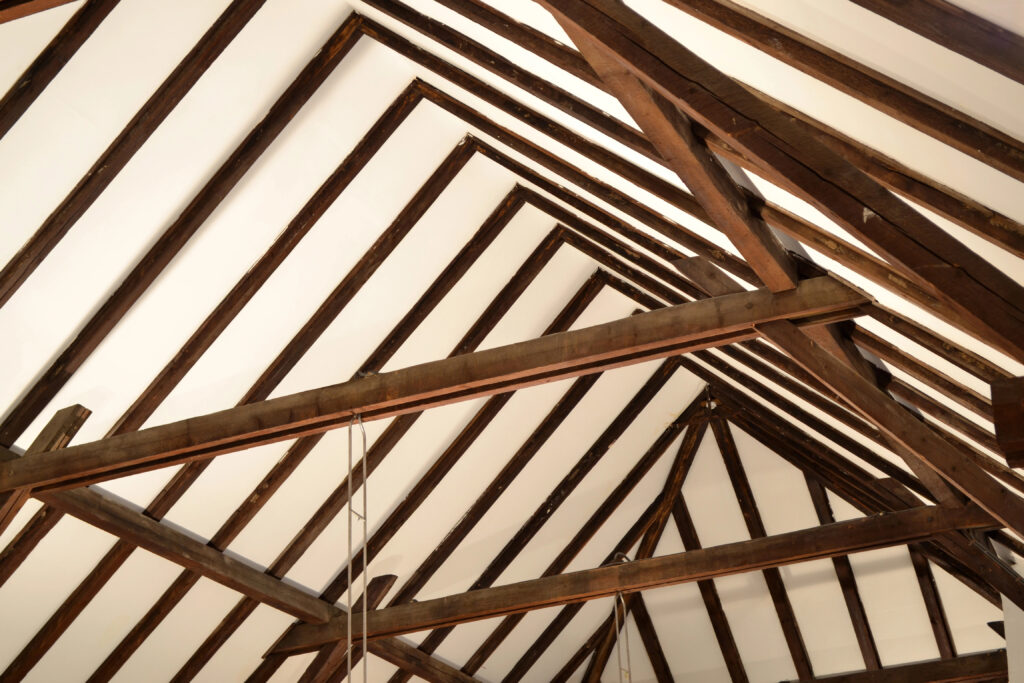 Un haut plafond en charpente à Gourdon, avec des poutres apparentes formant un motif géométrique, sur un fond blanc immaculé.