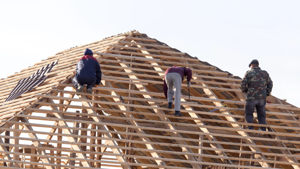 Par temps clair, trois ouvriers installent des poutres en bois sur le toit d'une maison de charpente à Pradines en construction.