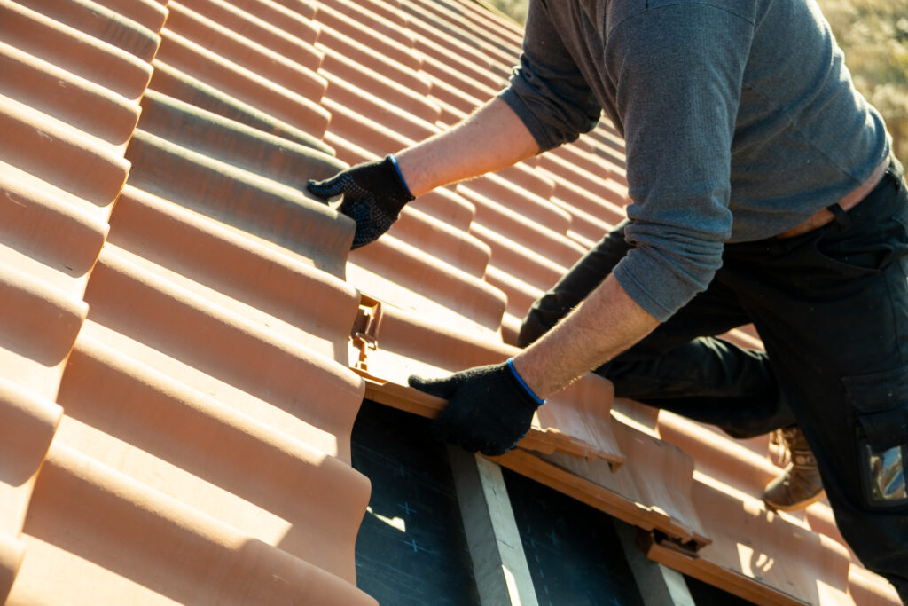 Un ouvrier portant des gants installe méticuleusement des tuiles de couleur terre cuite sur un toit en pente, démontrant le savoir-faire souvent observé dans la couverture à Pradines.