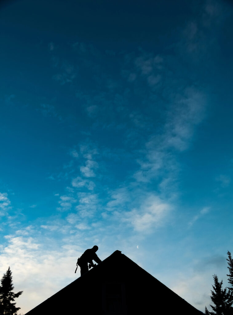 Personne silhouettée travaillant sur un toit de couverture à Souillac contre un ciel bleu avec des nuages épars au crépuscule.