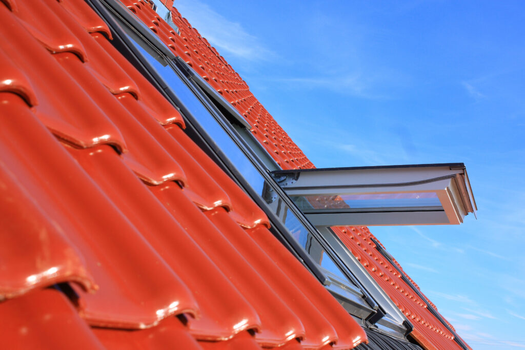 Vue rapprochée d'un toit de maison avec des tuiles d'argile rouge et une lucarne ouverte, récemment achevée dans le cadre d'une pose de velux à Gourdon, le tout sous un ciel bleu clair.
