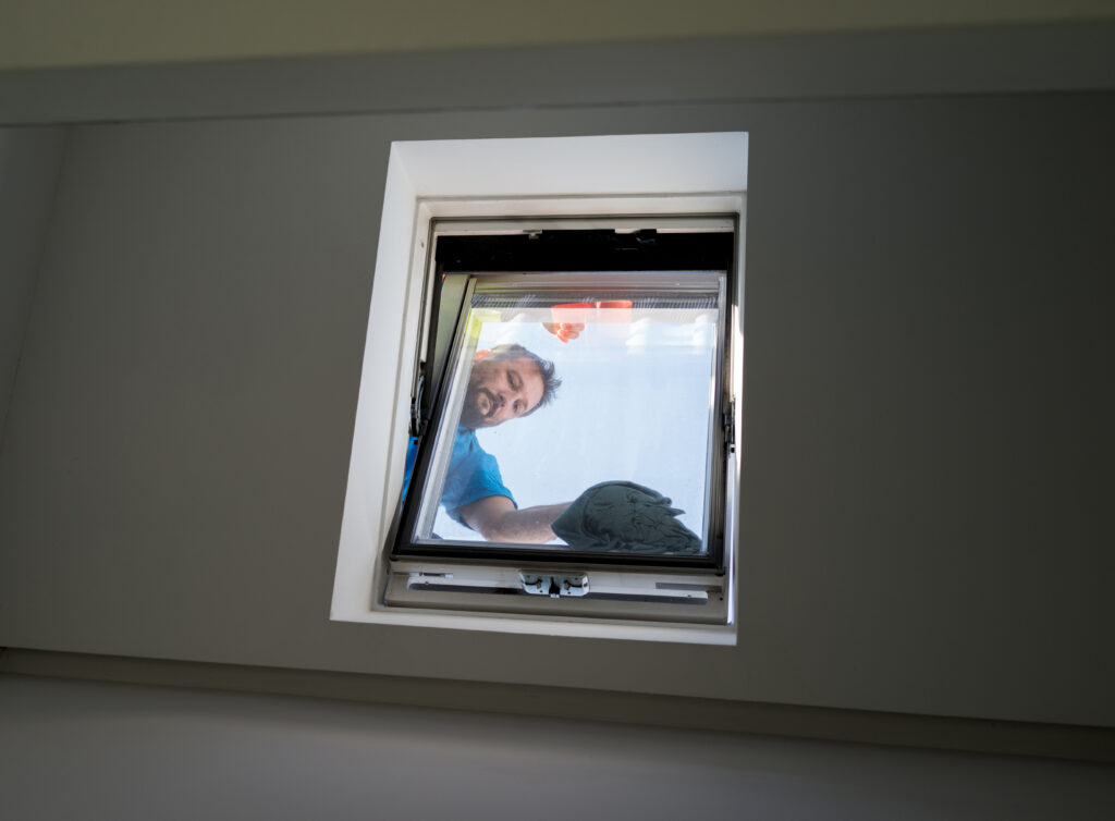 On peut voir une personne engagée dans la tâche méticuleuse de pose de velux à Saint-Céré nettoyer une lucarne de l'extérieur, tenant un outil de nettoyage et scrutant à travers la vitre.