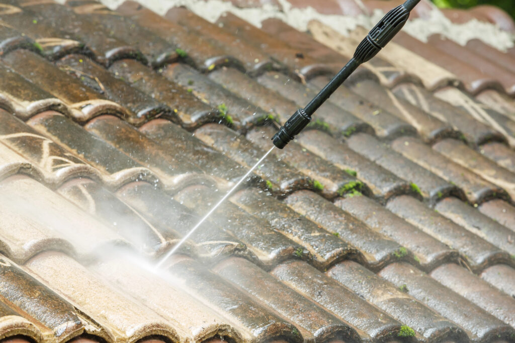 Un nettoyeur haute pression nettoyant la mousse et la saleté d'un toit de tuiles lors d'un nettoyage de toiture à Cahors.