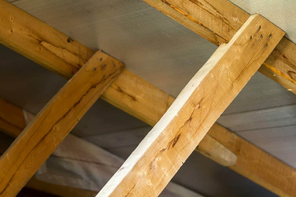 Gros plan de poutres en bois supportant un plafond avec vis et joints visibles.