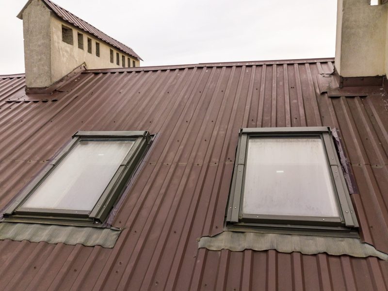 Une toiture en métal marron avec deux lucarnes, légèrement embuées, positionnées côte à côte. Le toit présente deux saillies verticales rectangulaires en arrière-plan.